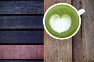 Une tasse de thé matcha latte avec un coeur dessiné sur une table en bois